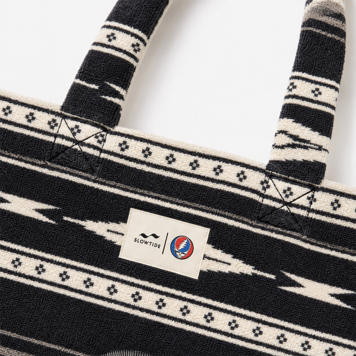 Beach bag with black and white pattern and circular blue-red logo on label.