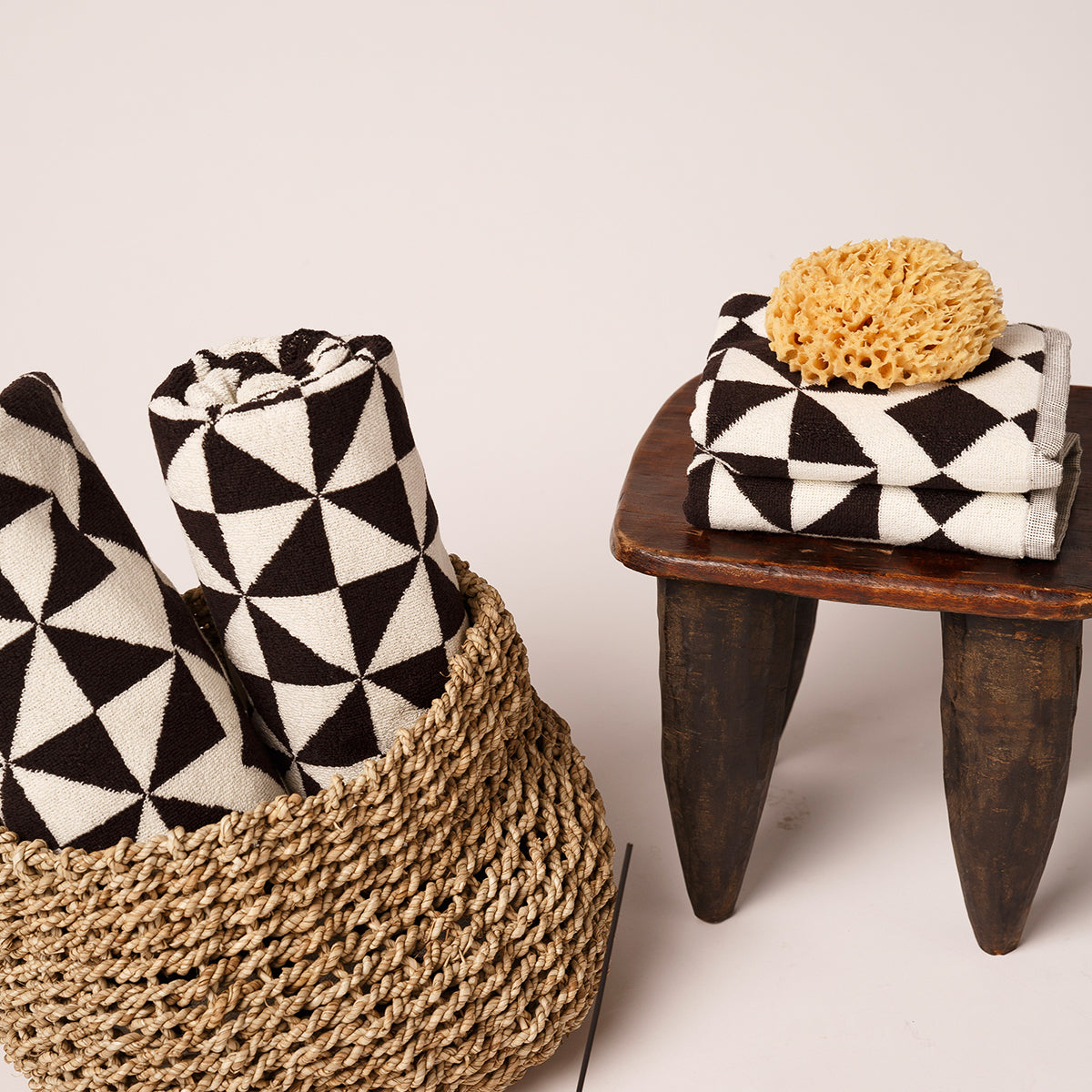 Cotton towels with black and white geometric pattern in basket and on stool, sea sponge nearby.