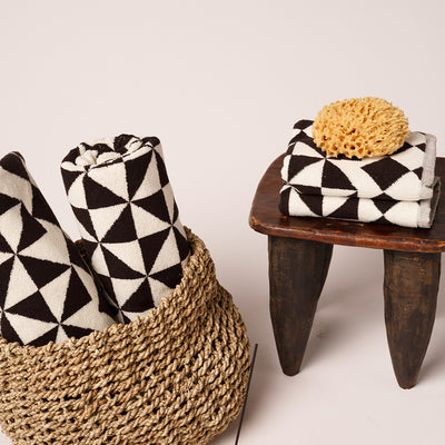 Cotton towels with black and white geometric pattern in basket and on stool, sea sponge nearby.