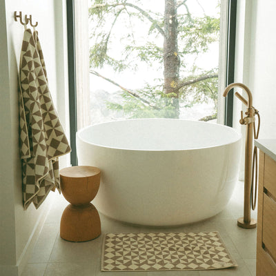 Round white freestanding bathtub with brass faucet and bath towel.