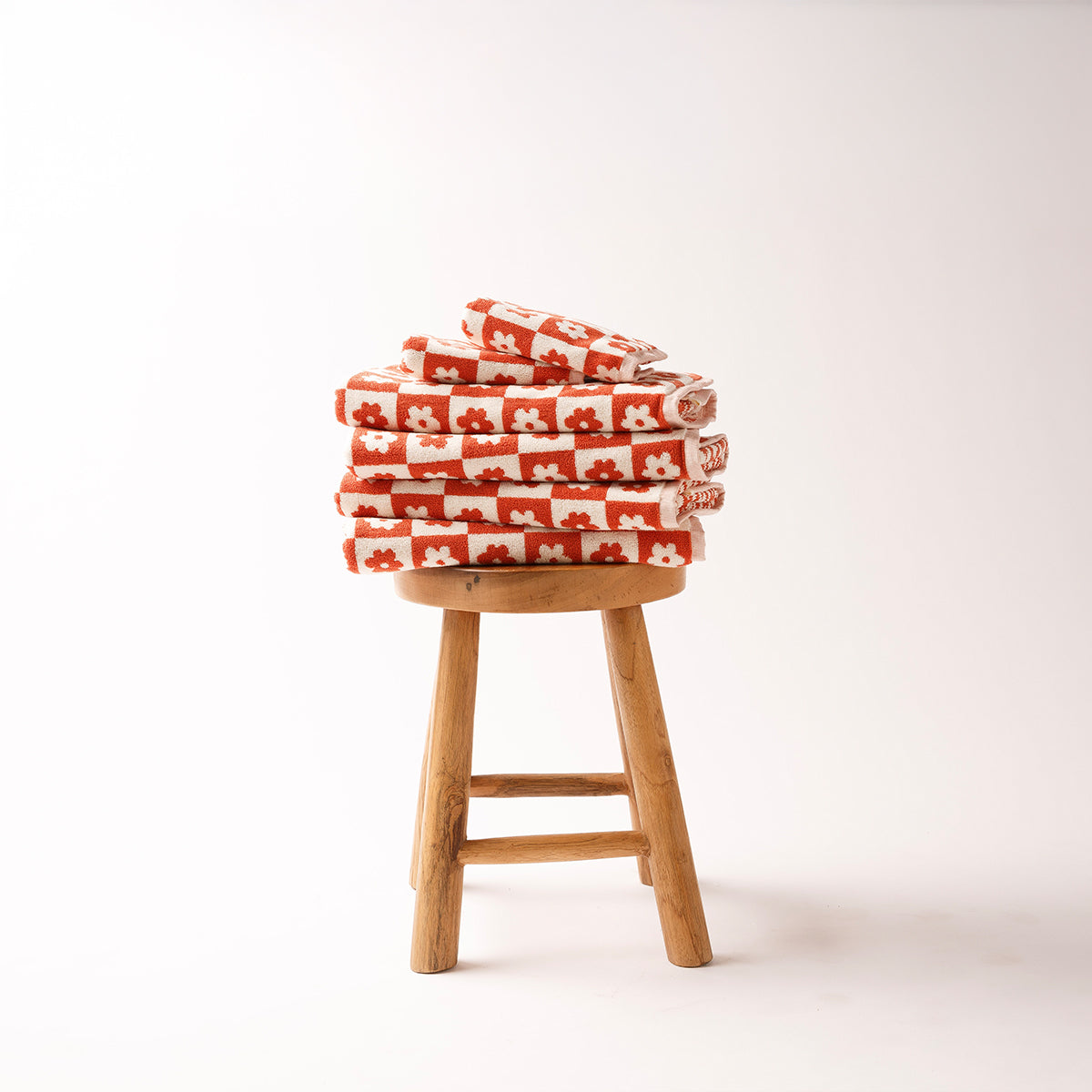 Bath towel stack with floral geometric pattern on wooden stool.