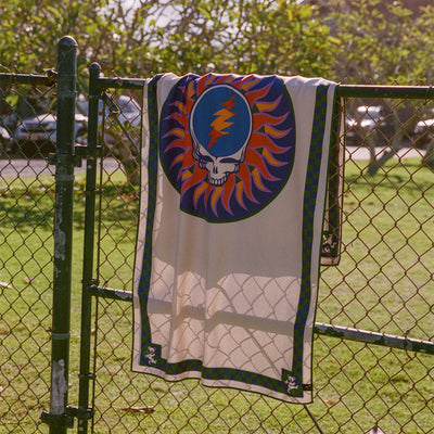 Sustainable towel with skull and lightning bolt print, displayed on a fence outdoors.
