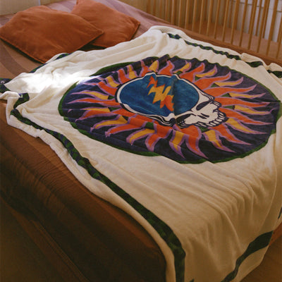 Oversized blanket with skull and lightning bolt pattern on bed with two brown pillows.