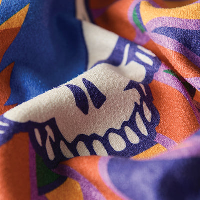 Microfiber travel towel with stylized skull and blue, orange, purple abstract pattern.