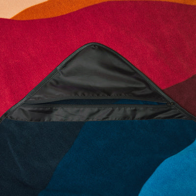 Fleece blanket with water-repellent finish, abstract pattern, and zippered storage pocket.