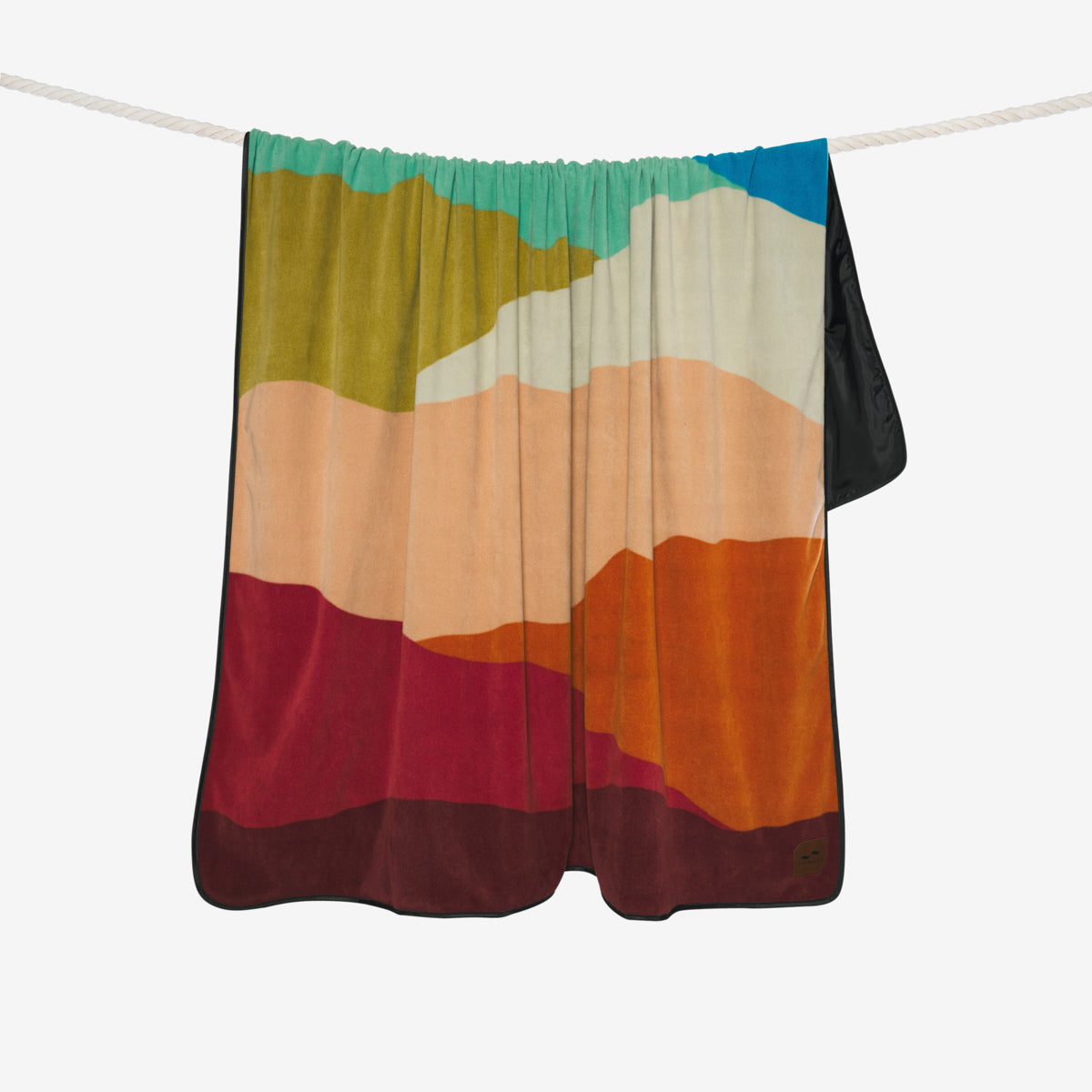 Water-repellent blanket with colorful abstract landscape print hanging on a rope.