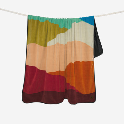 Water-repellent blanket with colorful abstract landscape print hanging on a rope.