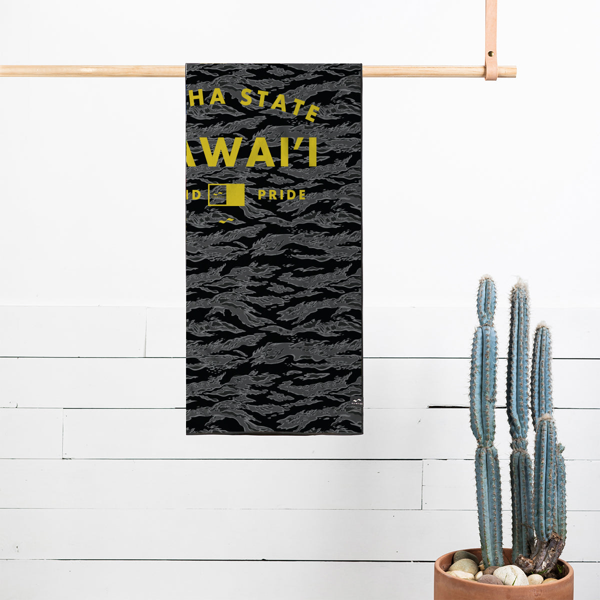 Quick-drying towel, black and gray with yellow text, shown near potted cactus for scale.