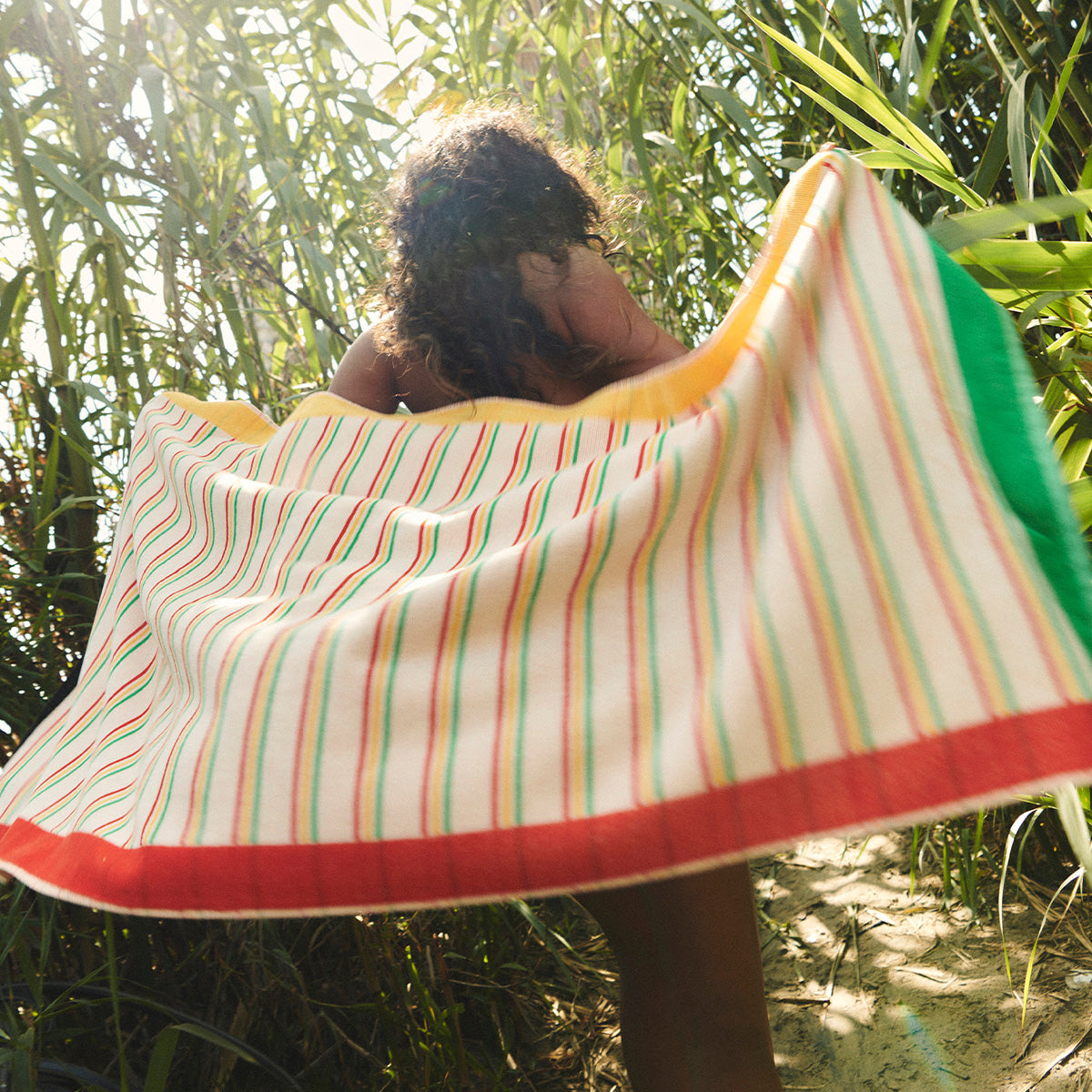 Striped sustainable cotton towel among tall green plants outdoors.