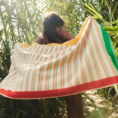 Striped sustainable cotton towel among tall green plants outdoors.