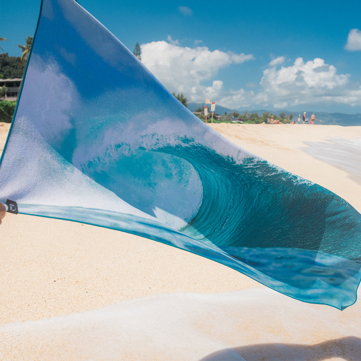 Beach towel, sand-free fabric with wave pattern, shown on sandy beach.