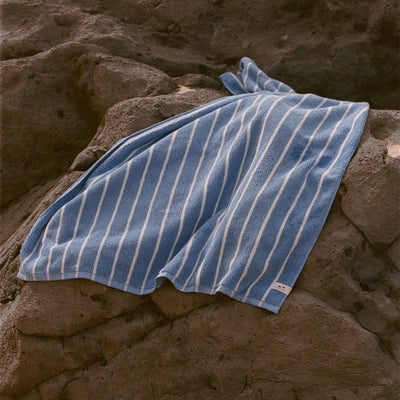 Quick dry towel with blue and white stripes displayed on brown rocks outdoors.
