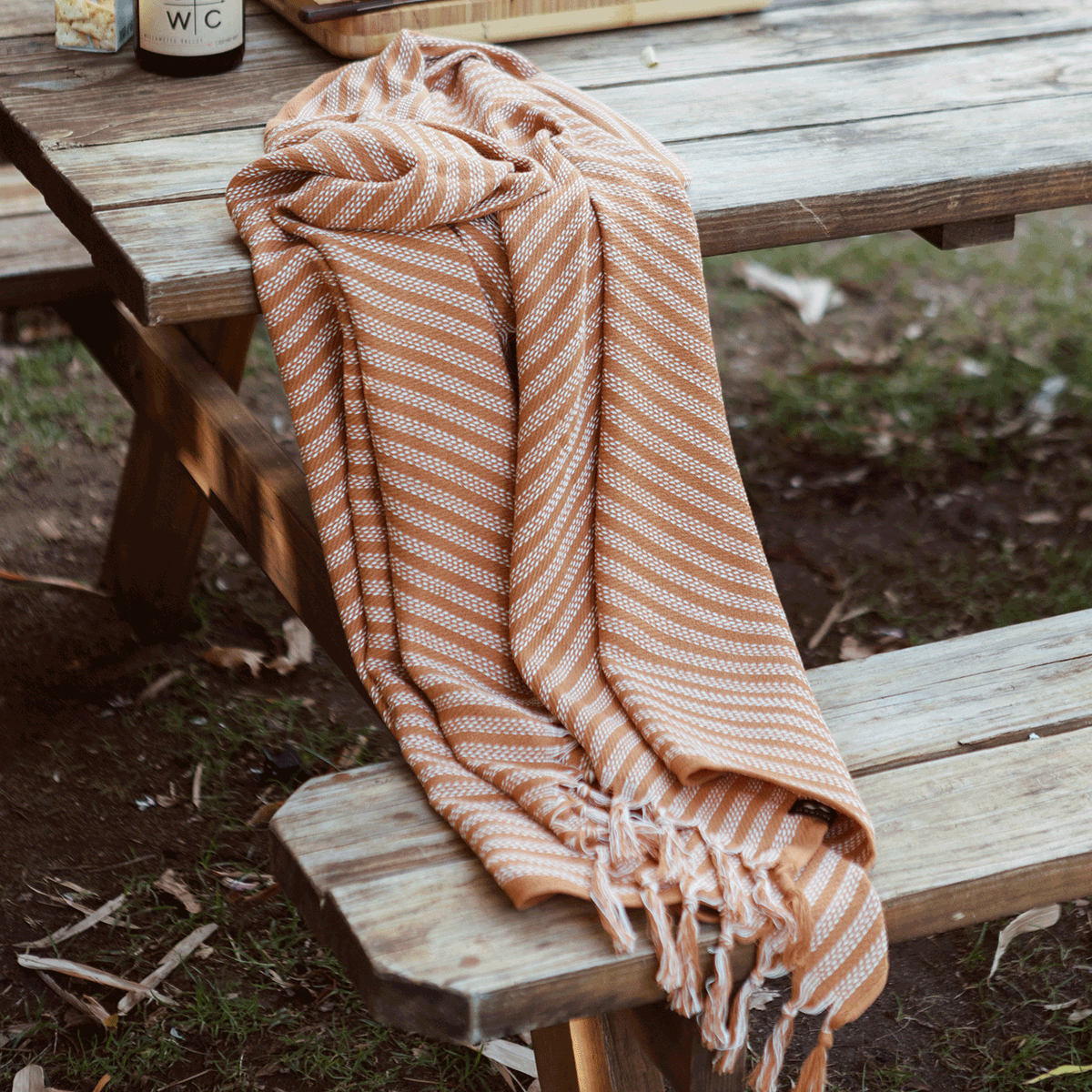 Beach towel, lightweight fabric, orange and white stripes, shown on a wooden picnic table.