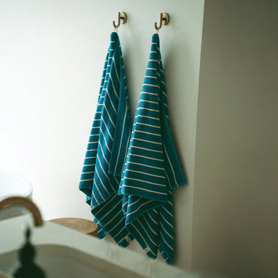 Plush teal striped bath towels hanging on wall hooks.