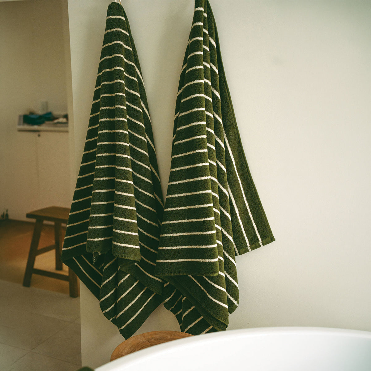 Plush bath towels in dark green with white horizontal stripes hanging on a wall.