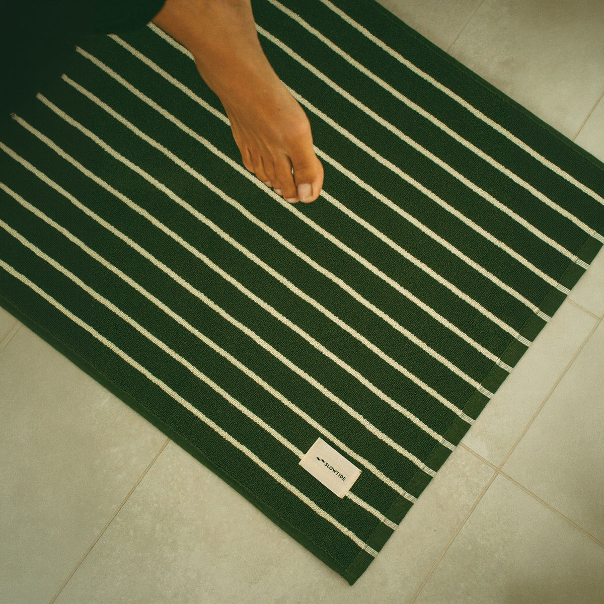 Cotton bath mat with green stripes on a tiled floor.