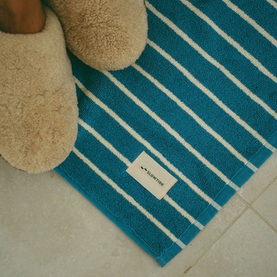 Cotton bath mat with blue and white stripes on a tiled floor.
