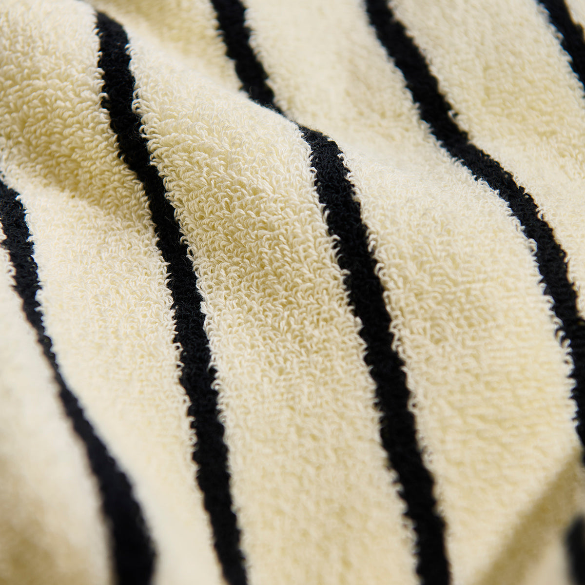 Cream towel, soft cotton texture with black stripes, close-up product detail.