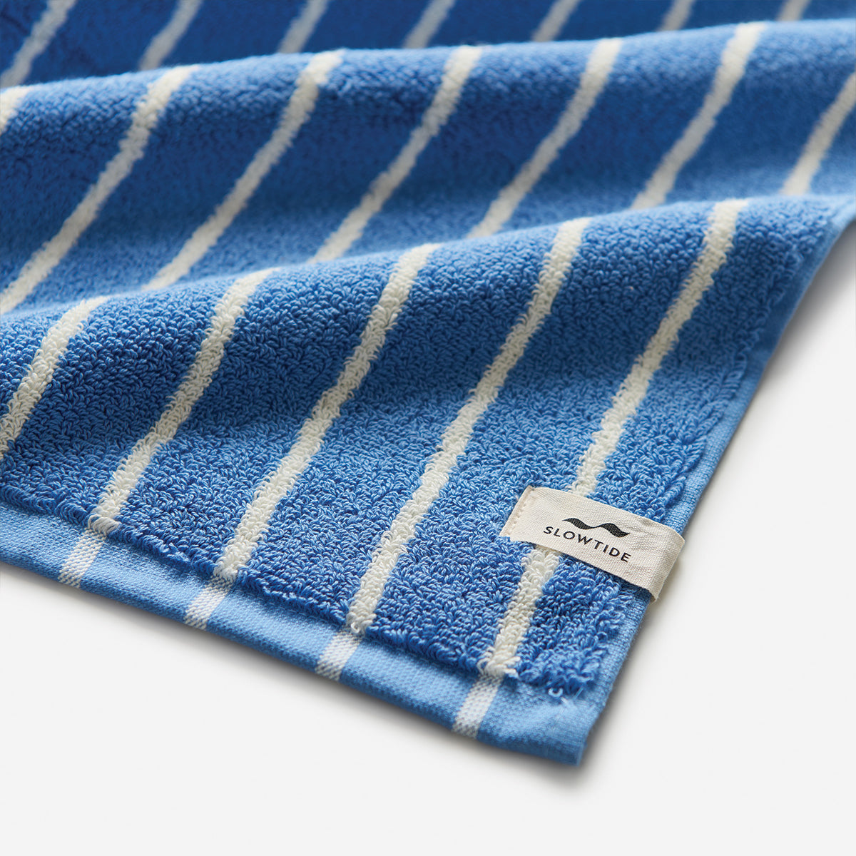 Blue beach towel with white stripes, sand resistant, close-up on tag corner.