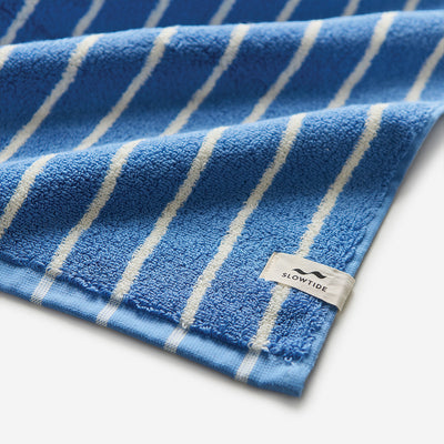 Blue beach towel with white stripes and corner tag.