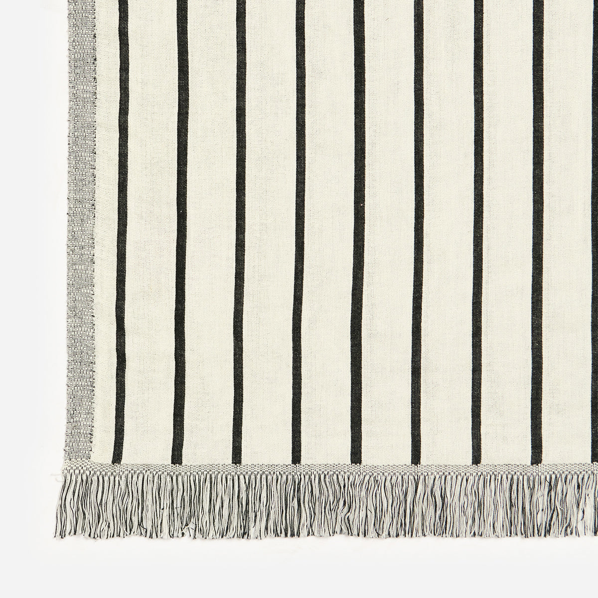 Cotton blanket with vertical black stripes and fringed edges on lightweight fabric.