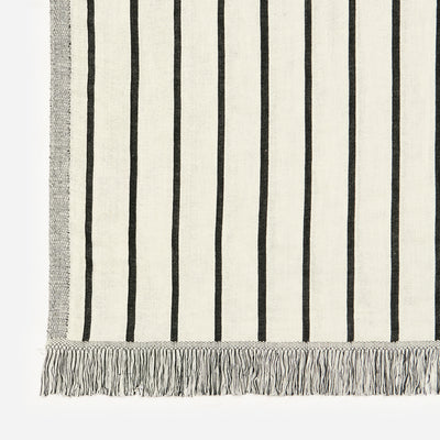 Cotton blanket with vertical black stripes and fringed edges on lightweight fabric.