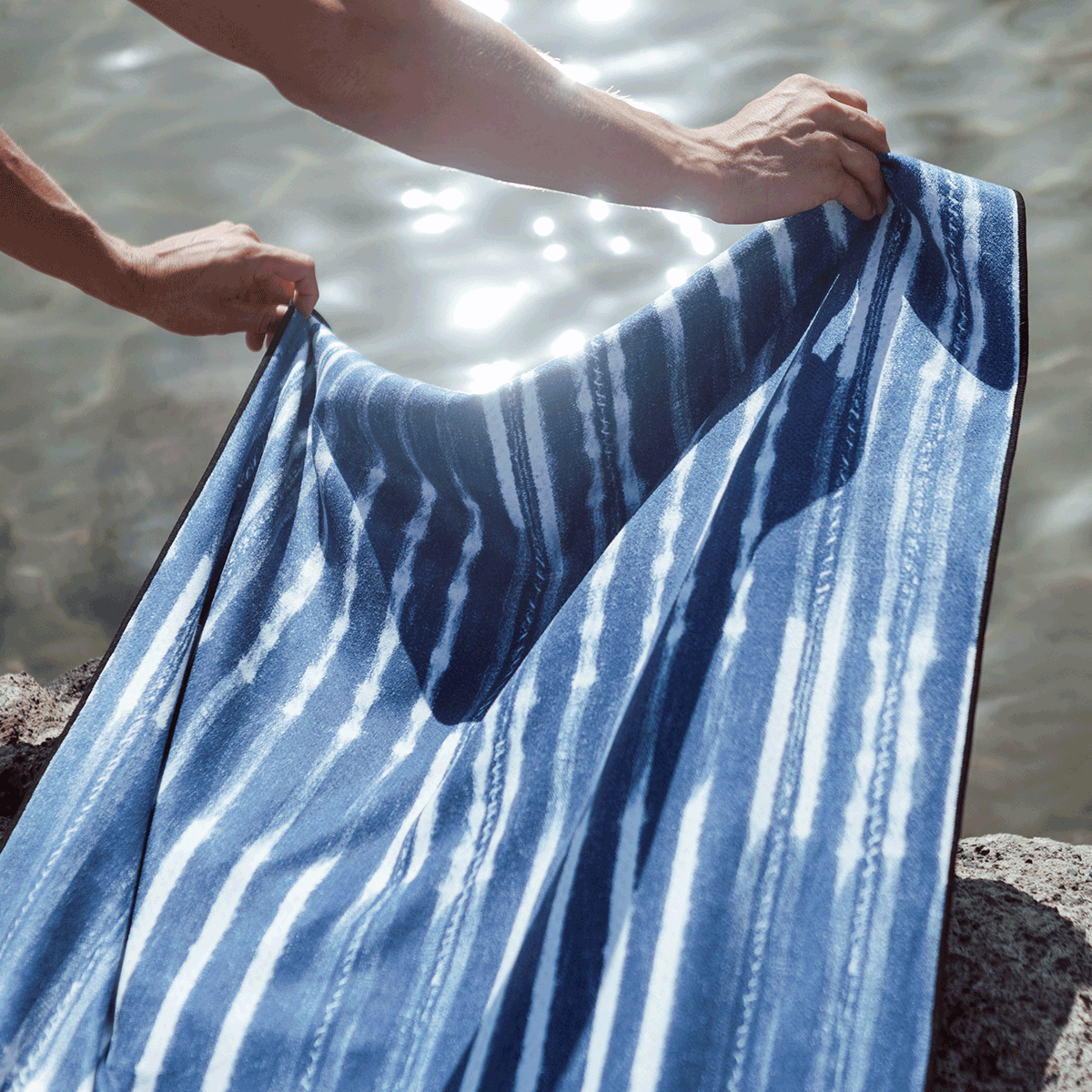 Beach towel, quick-drying fabric, blue and white stripes, shown over water.