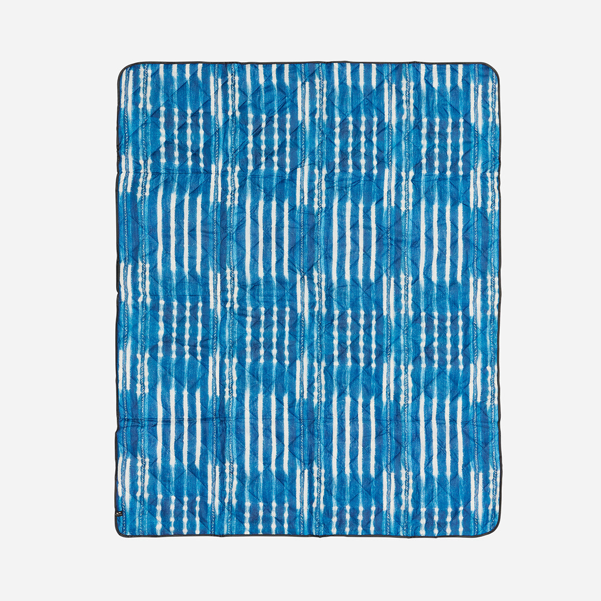 Quilted blanket in water-resistant fabric with blue and white ikat stripe tie-dye pattern.