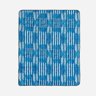 Quilted blanket in water-resistant fabric with blue and white ikat stripe tie-dye pattern.