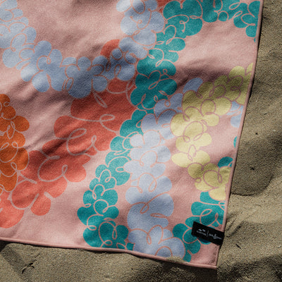Travel towel with floral pattern, quick-dry fabric, shown on sand in natural light.