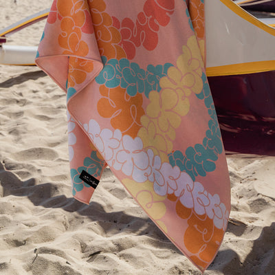 Travel towel with colorful floral pattern, quick-drying, displayed on a sandy beach boat.