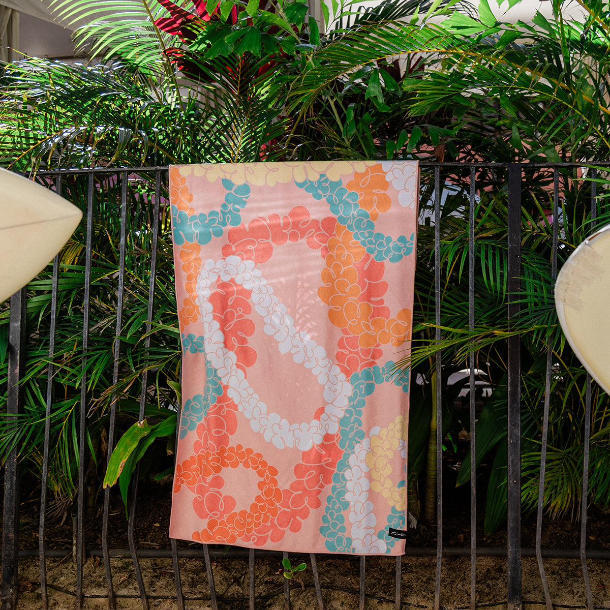 Quick-drying towel with colorful floral pattern displayed on black fence.