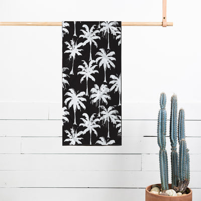 Recycled quick-dry towel with white palm tree print hanging by cactus and rocks.