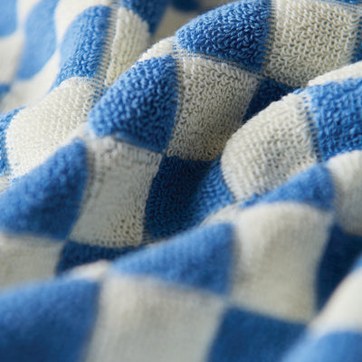 Bath towel in cotton terry with blue and white checkerboard pattern, close-up texture detail.