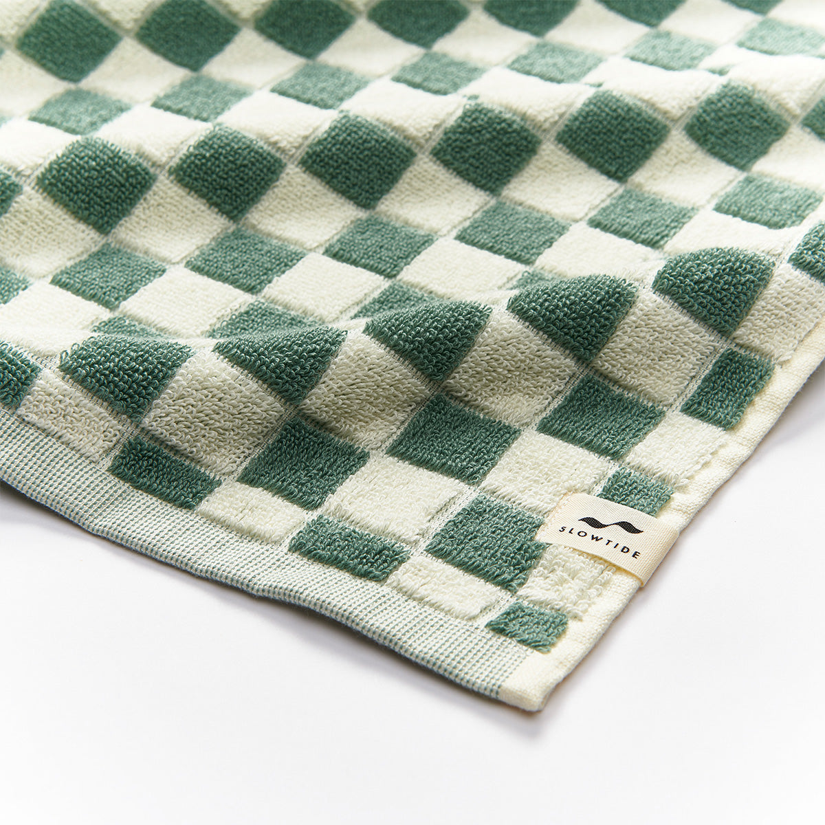 Cotton terry towel with green and cream checkerboard pattern, small label on edge.