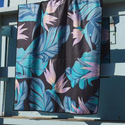 Quick-drying towel with blue and pink tropical leaves and flowers pattern.