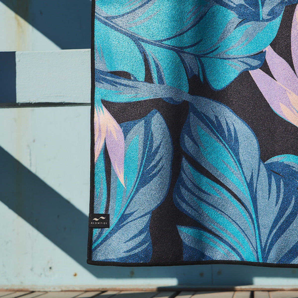 Quick-drying towel with blue and purple tropical leaf pattern on light blue wall.