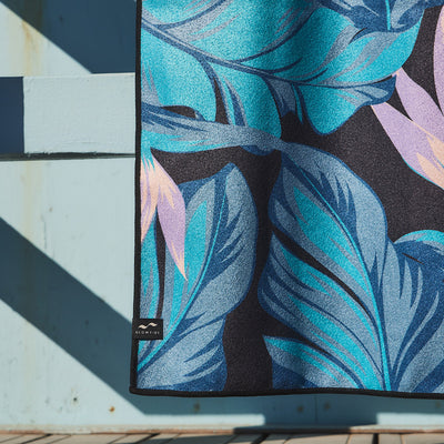 Quick-drying towel with blue and purple tropical leaf pattern on light blue wall.