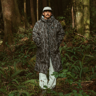 Patterned all-weather jacket and cap with green foliage print, outdoor setting.