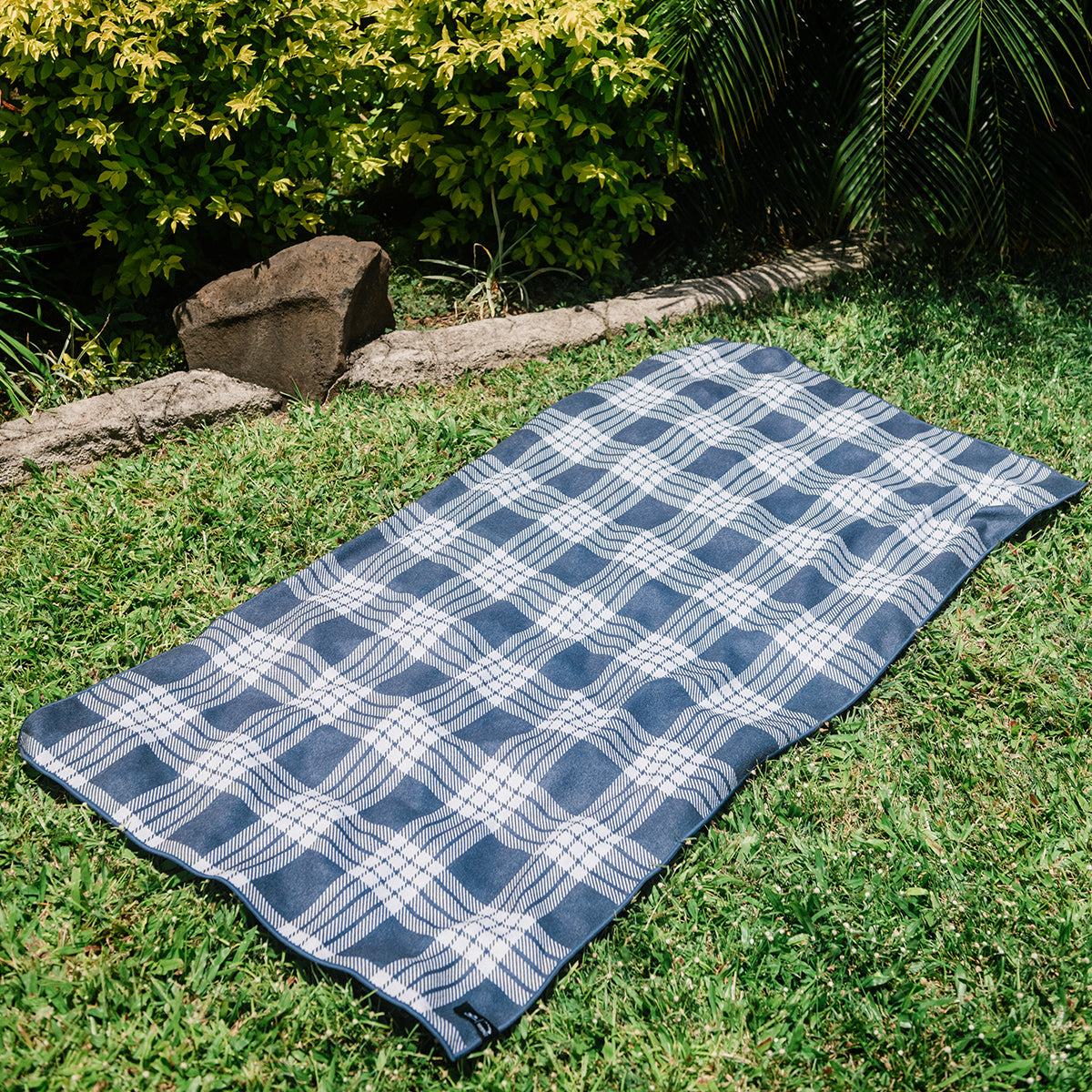 Travel towel with blue and white plaid pattern on green grass.