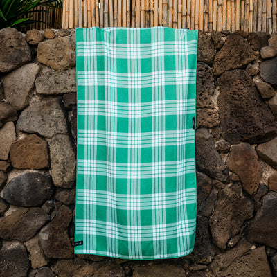 Quick-drying plaid towel with green and white pattern, displayed on a stone wall.