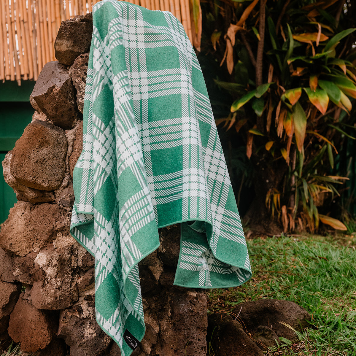 Quick-drying towel with green and white plaid pattern draped over a rock wall.