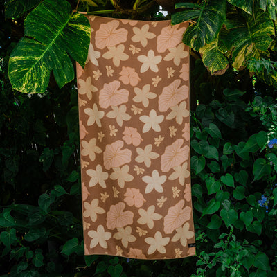 Brown sustainable towel with floral pattern hanging outside among green leafy plants.