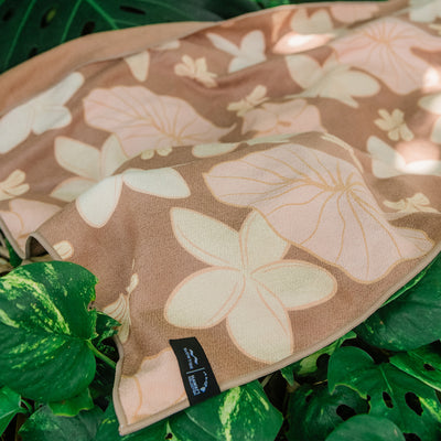 Quick-drying beige towel with floral pattern on green tropical leaves.