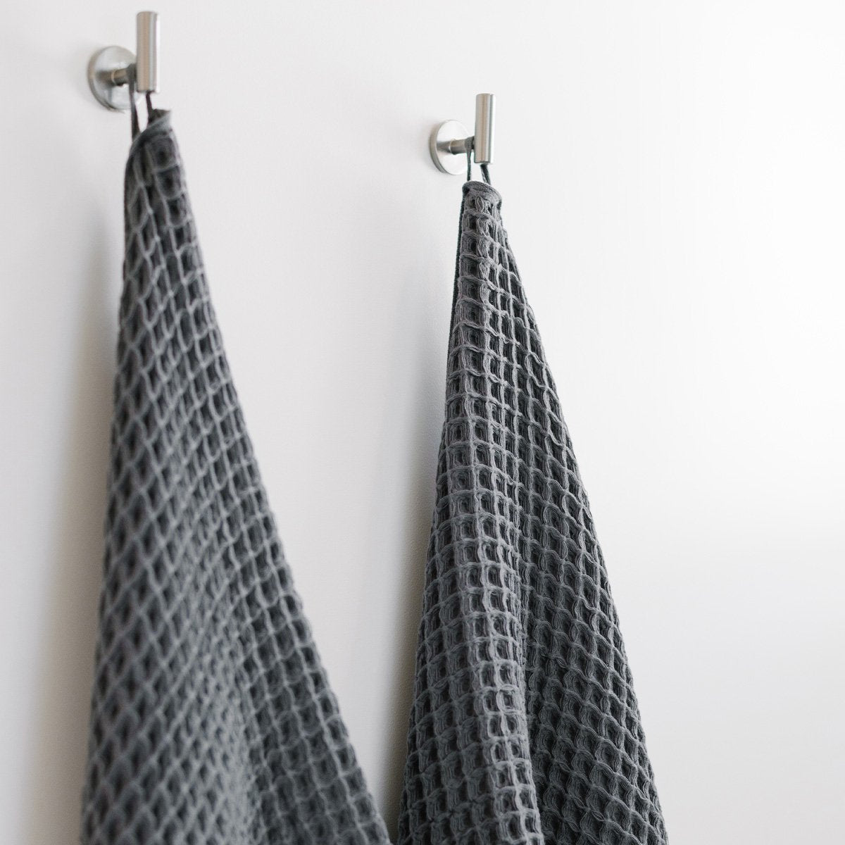 Gray waffle bath towels, sustainable cotton, hanging on silver hooks.