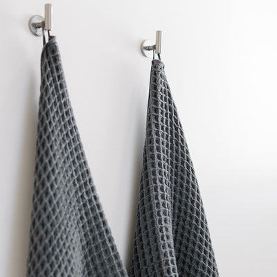 Gray waffle bath towels, sustainable cotton, hanging on silver hooks.