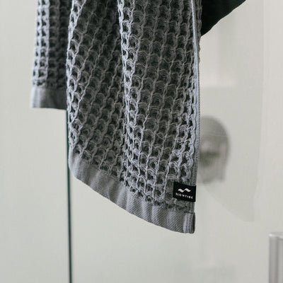 Gray waffle bath towel with textured pattern on a glass surface.
