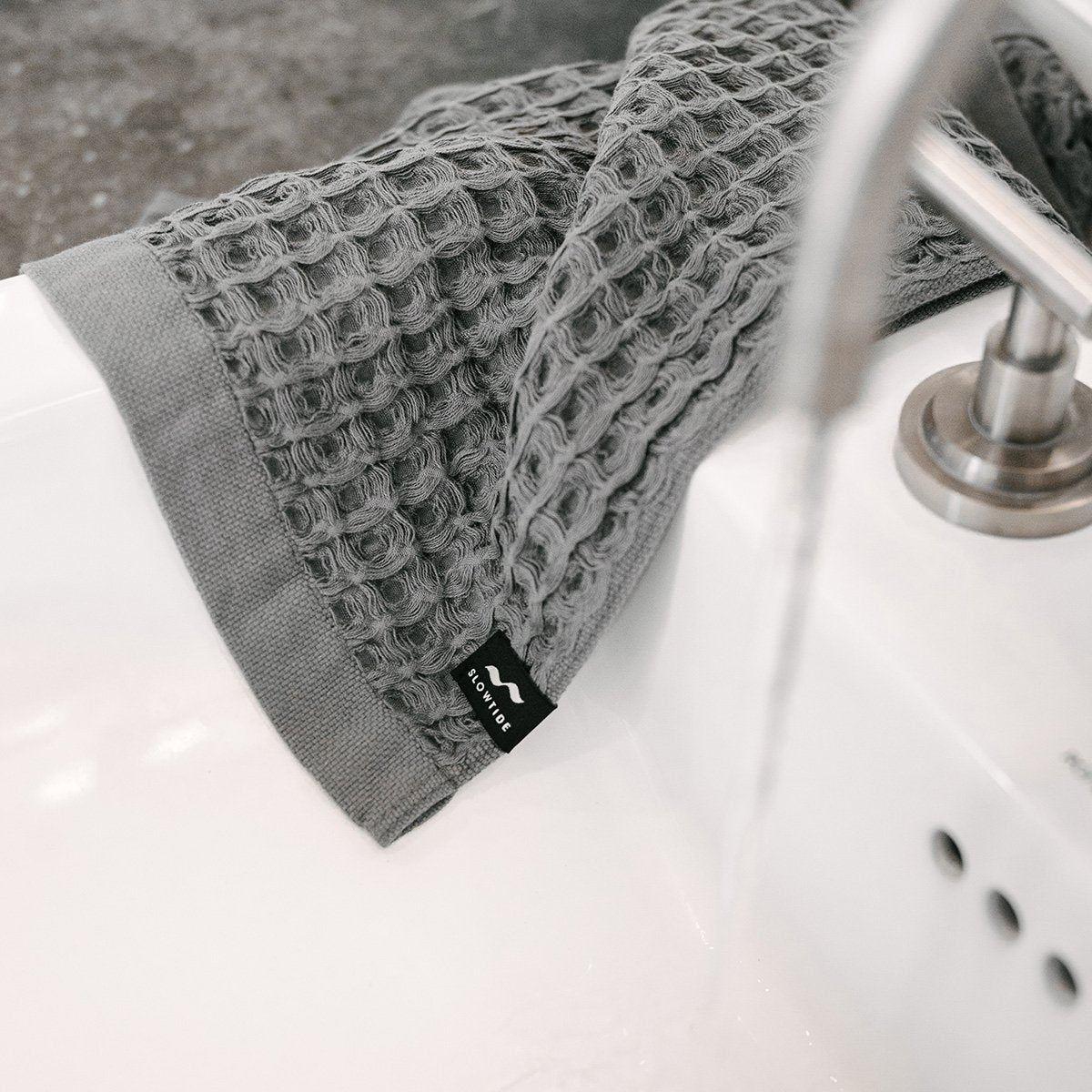 Absorbent towel with textured weave on white sink under running water.