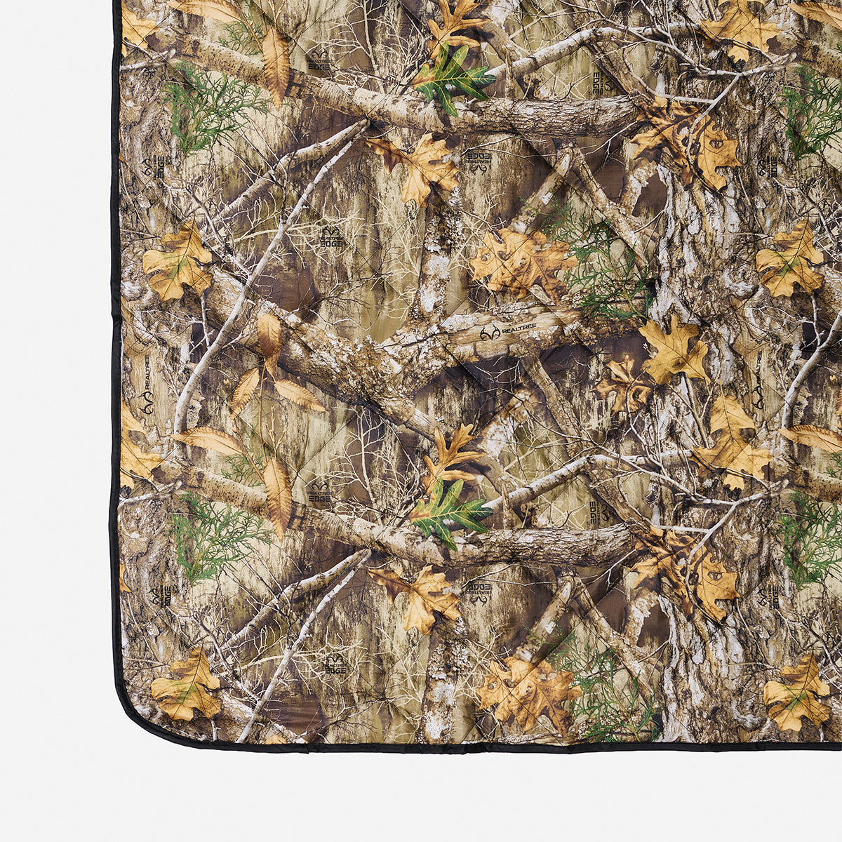 Quilted packable blanket with photorealistic leaf and branch camo pattern for outdoor use.