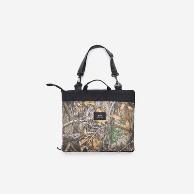 Tote bag with camo print, black handles, and small front logo patch.